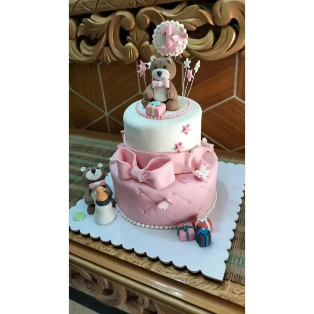 Two-tier birthday cake with teddy bear topper and bow detail